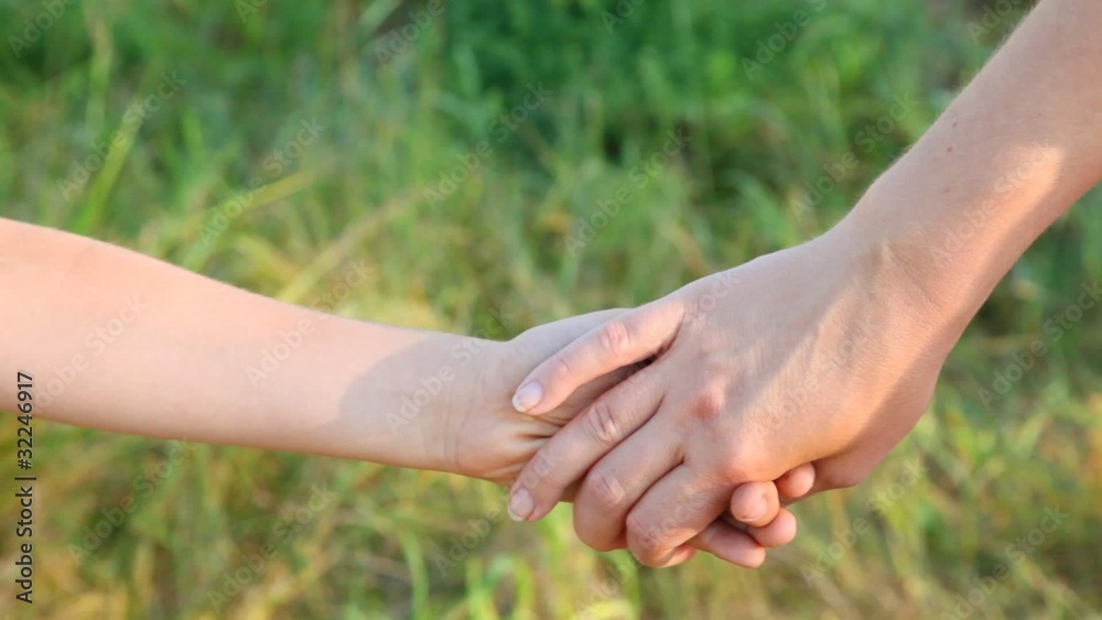 joined hands of mother and little daughter, grass in background joined hands of mother and little daughter, grass in background