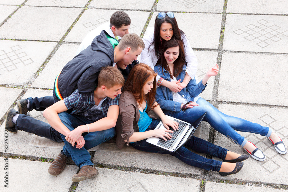 Group of male and female students sitting with a laptop on stree