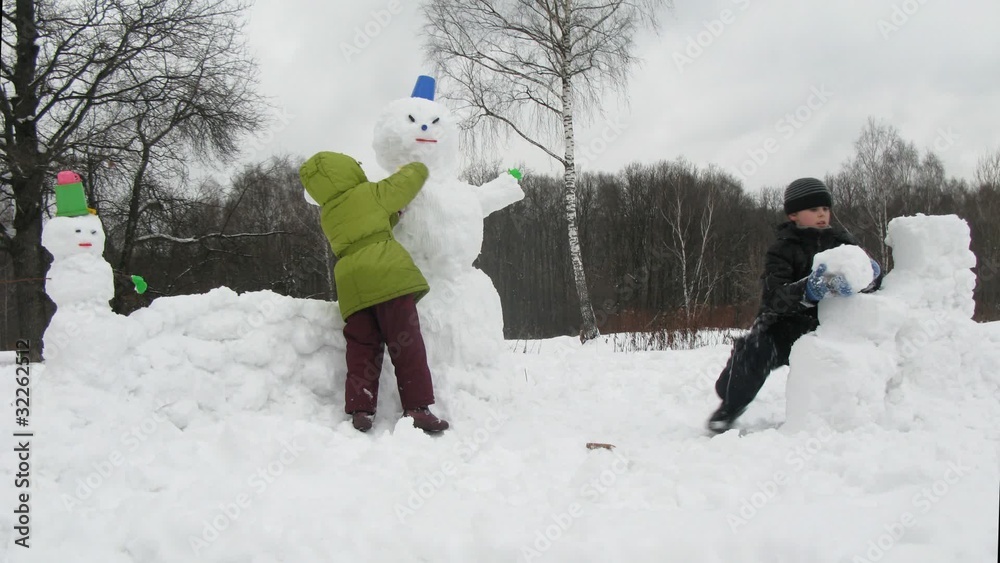 Two little kids play in snow sculpting snowman, time lapse