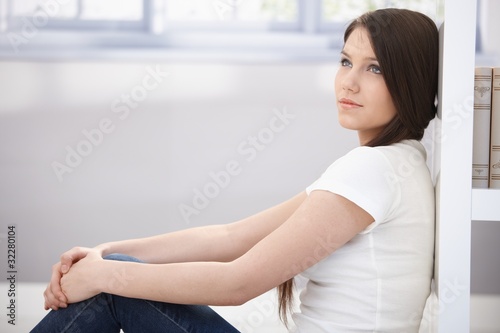 Daydreaming young woman sitting on floor