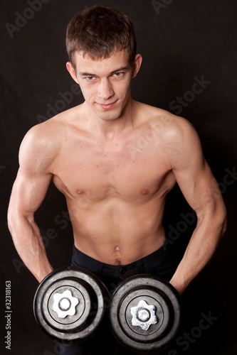 energetic naked man lifting dumbbell against black background © yurmary