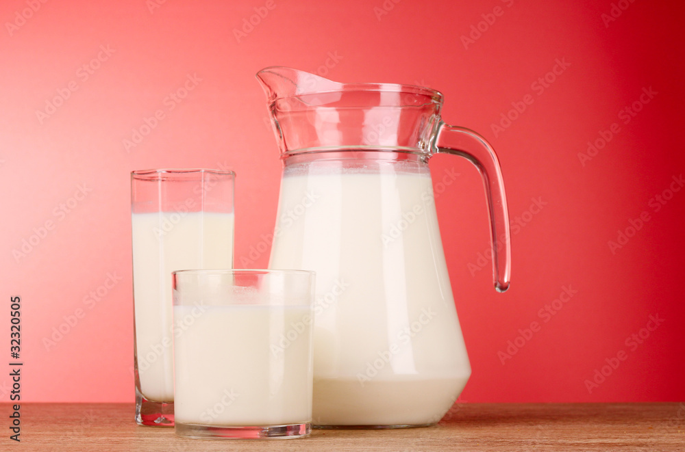 Pitcher and Glass with milk on red background Pitcher and Glass with milk on red background