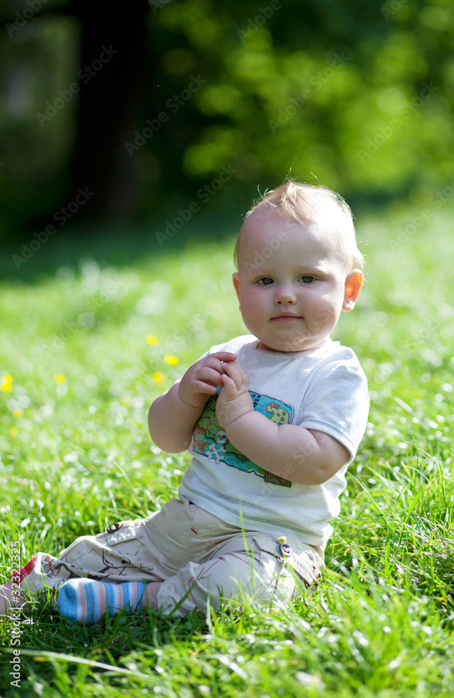 Adorable little boy sitting on the grass outdoors Adorable little boy sitting on the grass outdoors