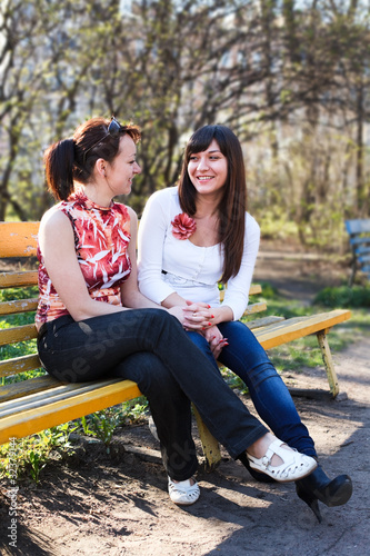 Two young beautiful women chatting on a park bench