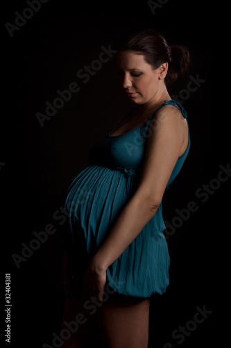 Pregnant woman in blue dress looking her stomach