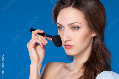 Young female applying mineral powder on her face with brush