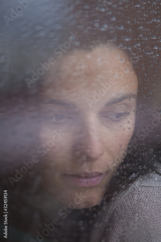 Traurige Frau hinter Fenster mit Regentropfen