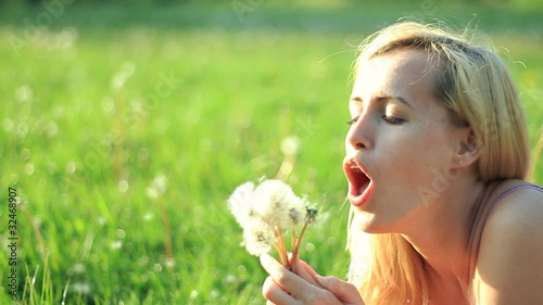girl blowing on white dandelions on green field, slow motion