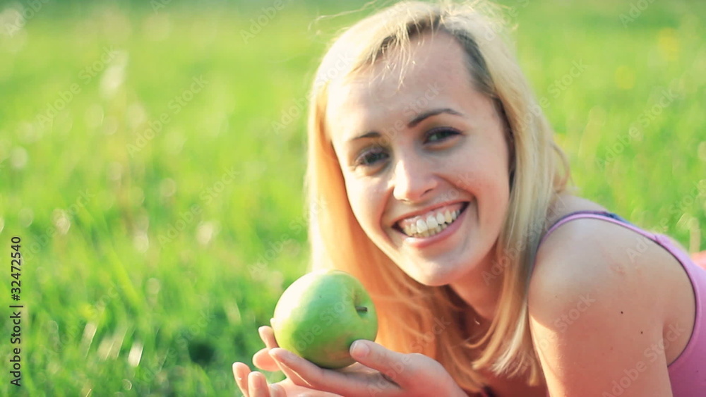 Young attractive woman lying on grass and holding apple Young attractive woman lying on grass and holding apple