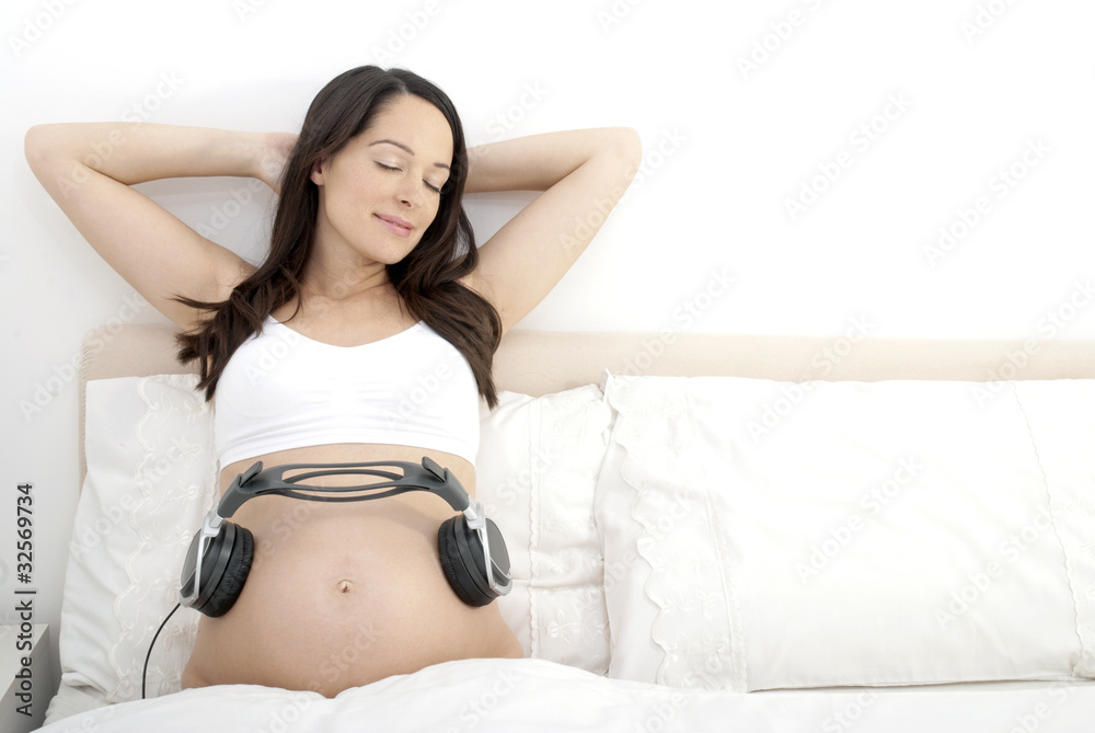 Pregnant woman playing music to baby in bed Pregnant woman playing music to baby in bed