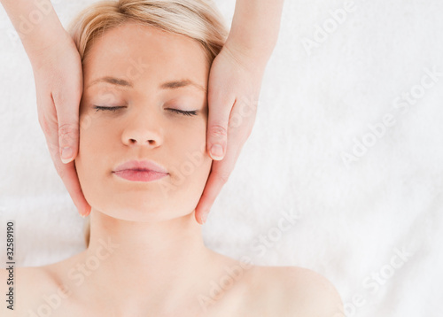 Delighted blond-haired woman getting a massage on her face