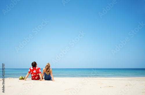 Young lovers sitting on warm sand at sunny day and looking to somewhere