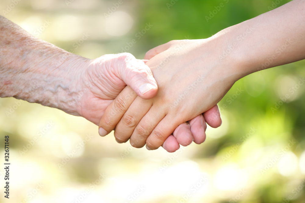 Senior and young women holding hands over shiny green background Senior and young women holding hands over shiny green background