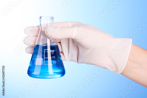 beaker with blue liquid on hand with blue background