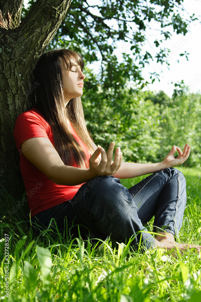 Young brunette girl in red shirt siting near tree and meditating Young brunette girl in red shirt siting near tree and meditating
