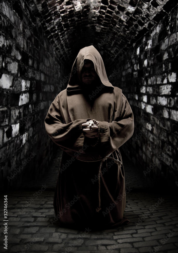 Praying monk in dark temple corridor - obrazy, fototapety, plakaty 