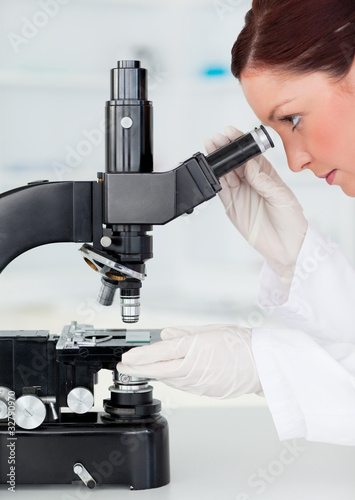 Beautiful red-haired scientist looking through a microscope