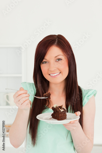 Pretty red-haired woman eating some cake in the kitchen