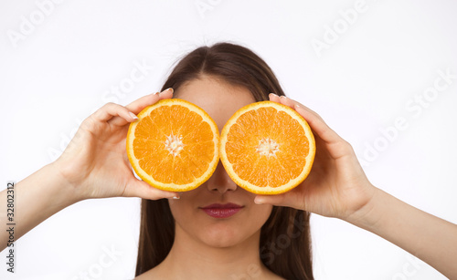 Young woman holding two halves of orange in front of her eyes