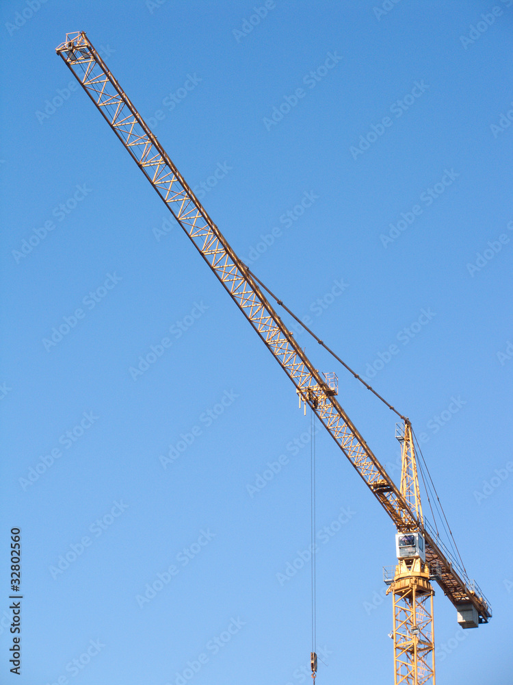 Yellow construction hoisting crane on clear blue sky vertical