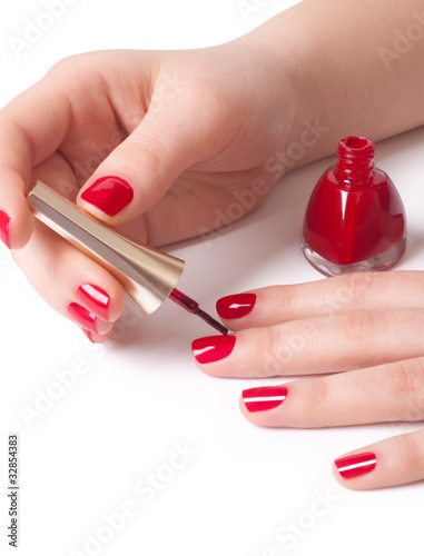 Manicurist applying red nail polish on female fingers