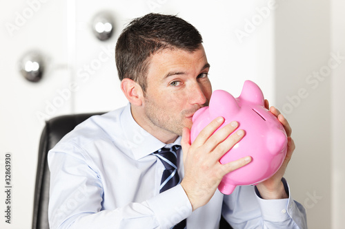 young man in office kissing a pink piggy bank