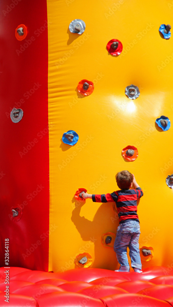 Fototapeta premium Kleiner Junge beim Spielen an einer aufblasbaren Kletterwand