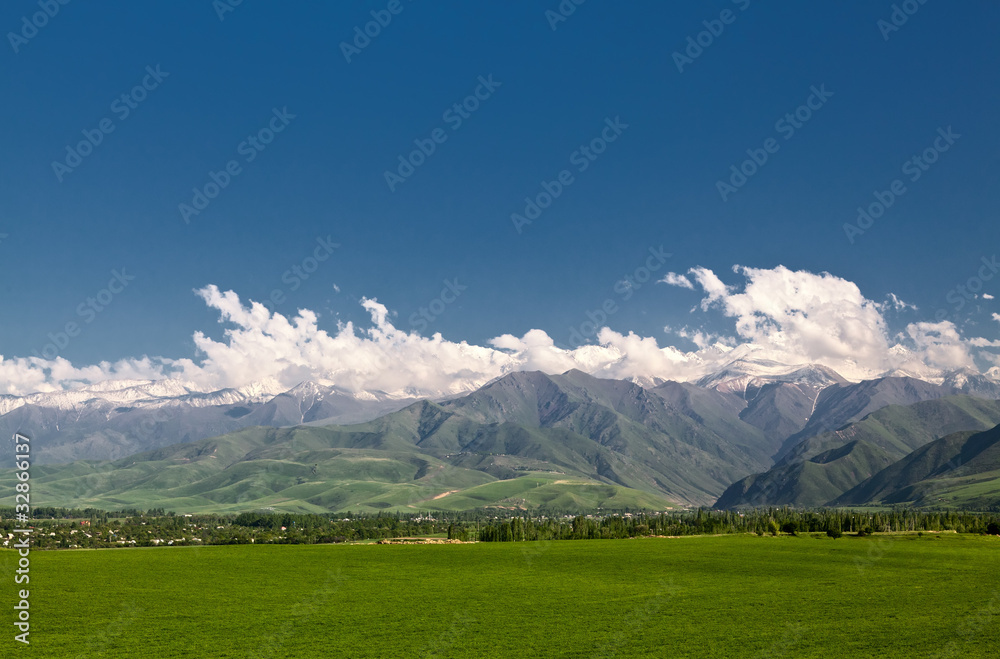 Panoramic mountain landscape with a  green field in the foregrou