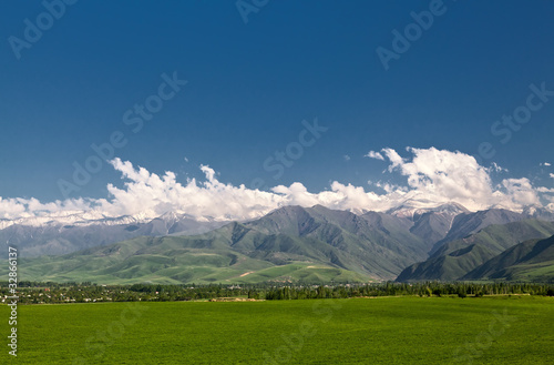 Panoramic mountain landscape with a green field in the foregrou