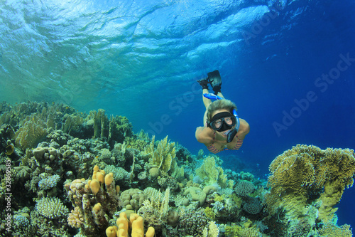 Beautiful Woman snorkeler dives down over a coral reef