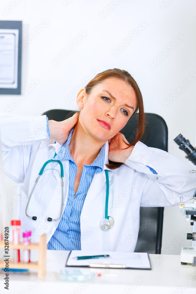 Tired doctor woman sitting at able and massaging her neck. Tired doctor woman sitting at able and massaging her neck.