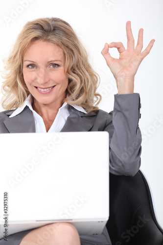 Blonde businesswoman with a laptop giving the OK sign