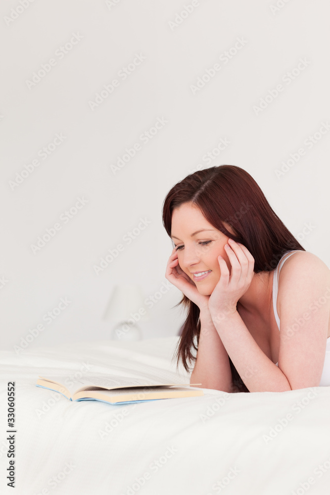 Pretty red-haired woman reading a book while lying on her bed Pretty red-haired woman reading a book while lying on her bed