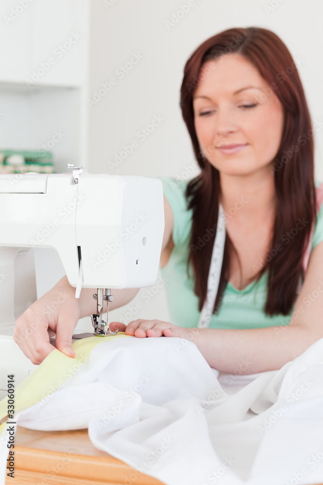 Beautiful red-haired female using a sewing machine in the living Beautiful red-haired female using a sewing machine in the living