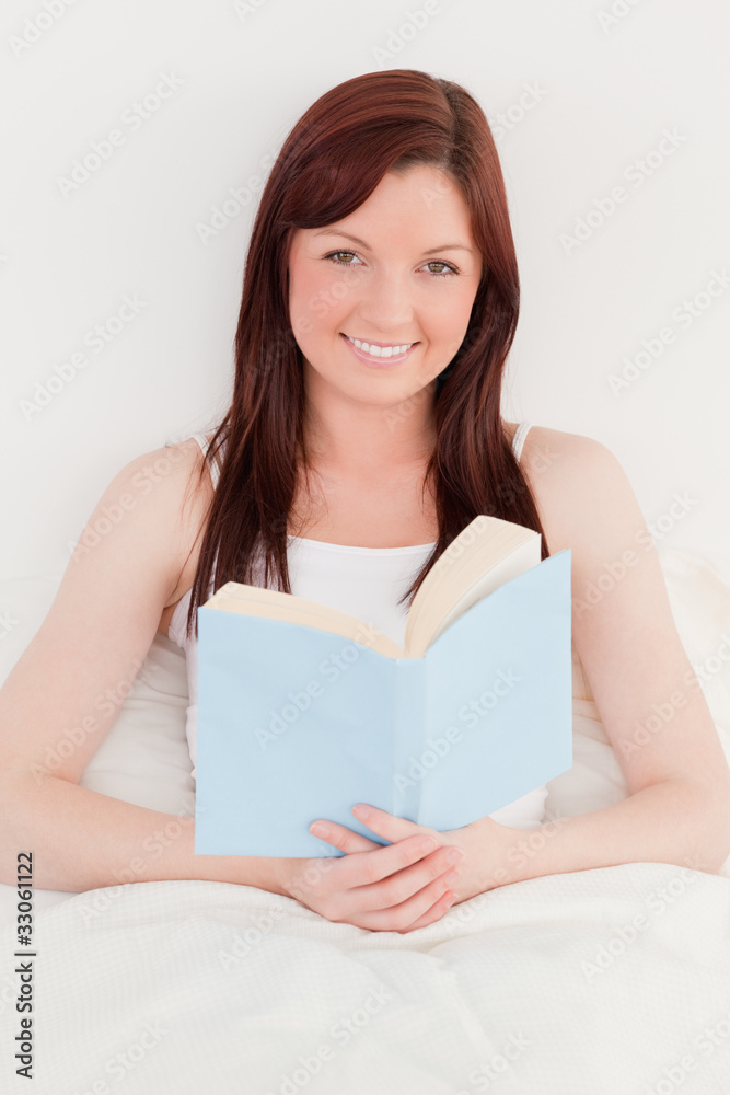 Good looking red-haired female reading a book while sitting on h Good looking red-haired female reading a book while sitting on h