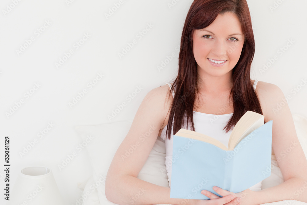Gorgeous red-haired female reading a book while sitting on her b Gorgeous red-haired female reading a book while sitting on her b