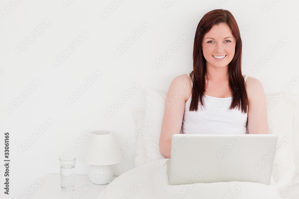 Attractive red-haired woman relaxing with her laptop while sitti Attractive red-haired woman relaxing with her laptop while sitti