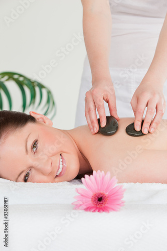 Smiling woman receiving a hot stone massage and a pink gerbera