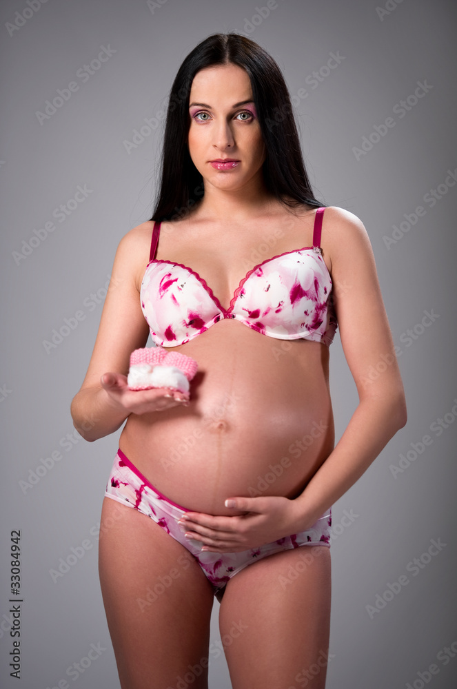 Naklejka premium Lovely pregnant woman holding a pair of pink baby booties