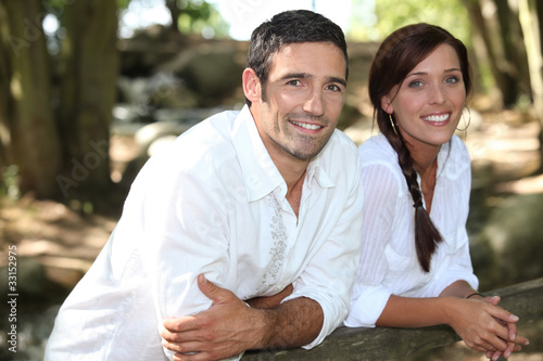 Couple in white leaning on a wooden fence