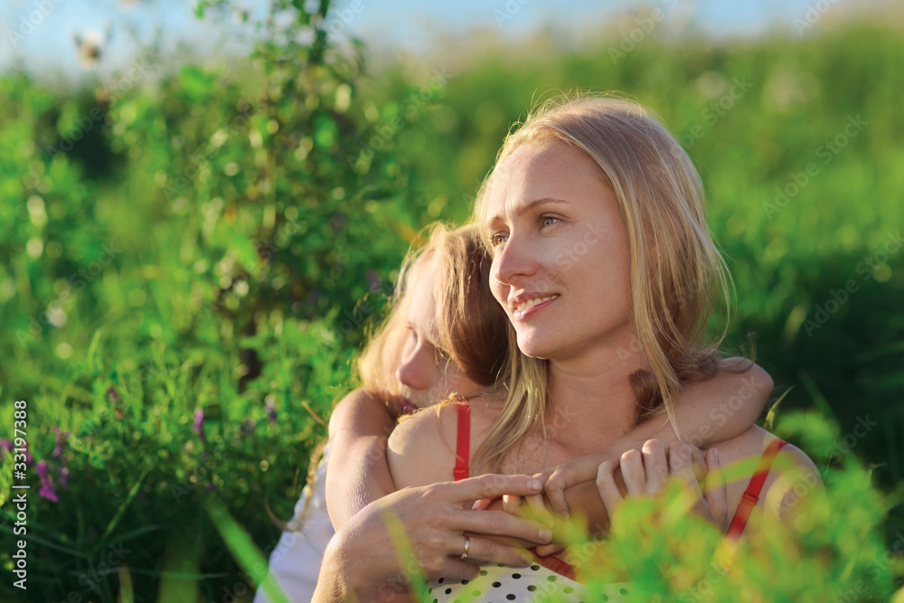 Beautiful mother and daughter sitting on green lush grass meadow Beautiful mother and daughter sitting on green lush grass meadow