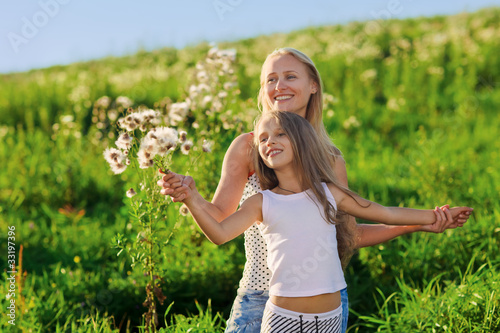 Beautiful mother and daughter family playing on meadow in sunset