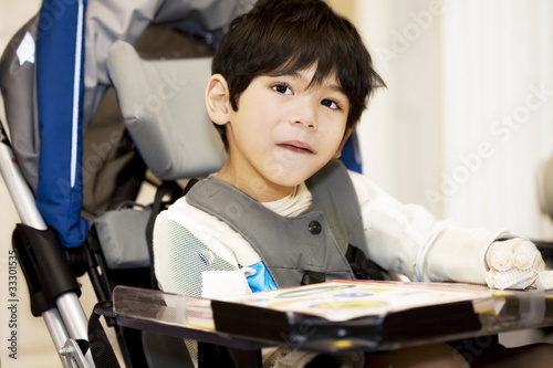 Disabled four year old boy studying or reading in wheelchair photo