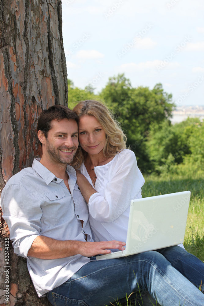 Couple sat in field with laptop computer Couple sat in field with laptop computer