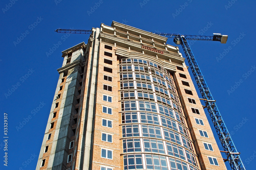 Fototapeta premium Building crane and building under construction against blue sky