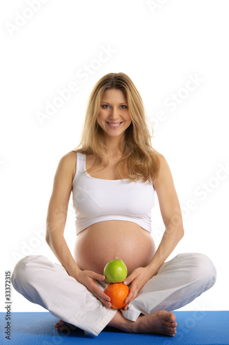 Pregnant woman practicing yoga and keeps fruit