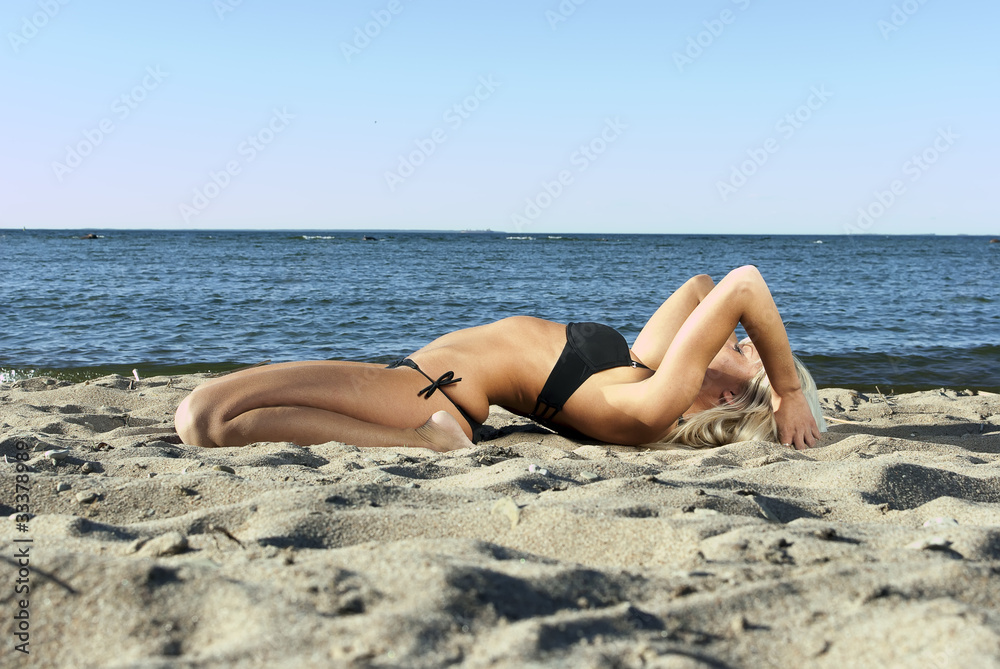 blonde girl in a black suit lying on the beach and meditate