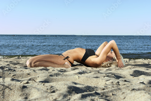 blonde girl in a black suit lying on the beach and meditate