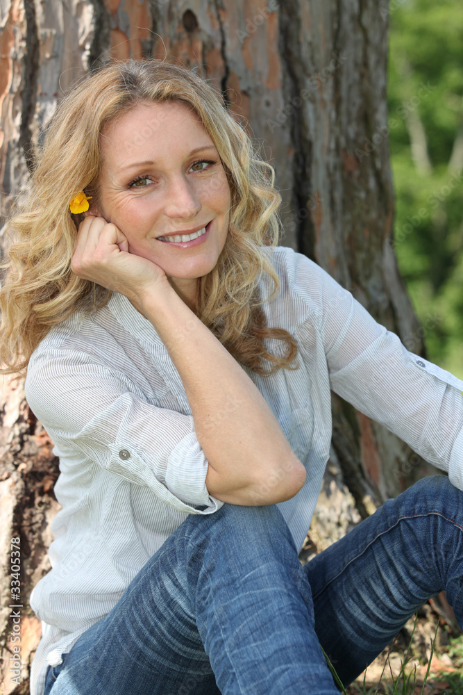 Woman with yellow flower in her hair sitting in front of a tree Woman with yellow flower in her hair sitting in front of a tree
