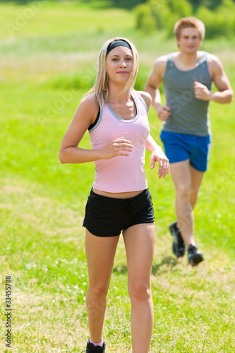 Fototapeta Naklejka Na Ścianę i Meble -  Sportive young couple jogging meadows sunny summer
